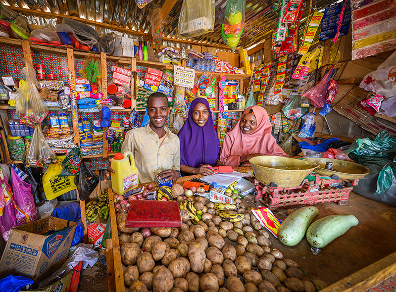 A man and two women smile as they stand inside the store they manage filled with various goods and produce.