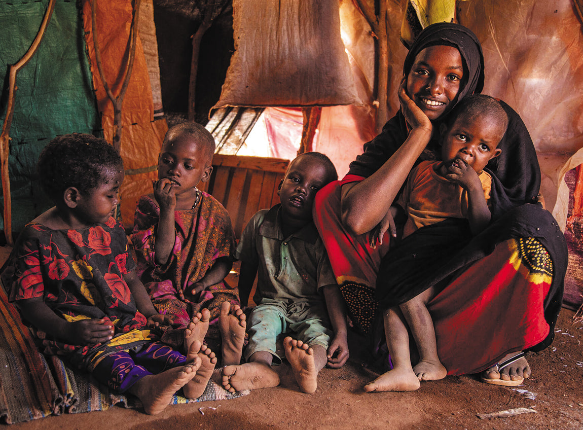 A woman and her four children sit on the ground under a tent filled with textiles.