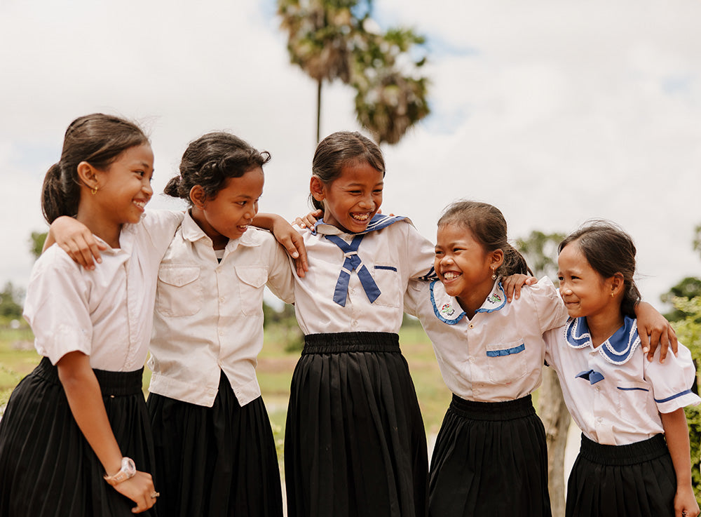 Five girls wearing blue and and white school uniform laugh and smile as they put their arms on
each other's shoulders.