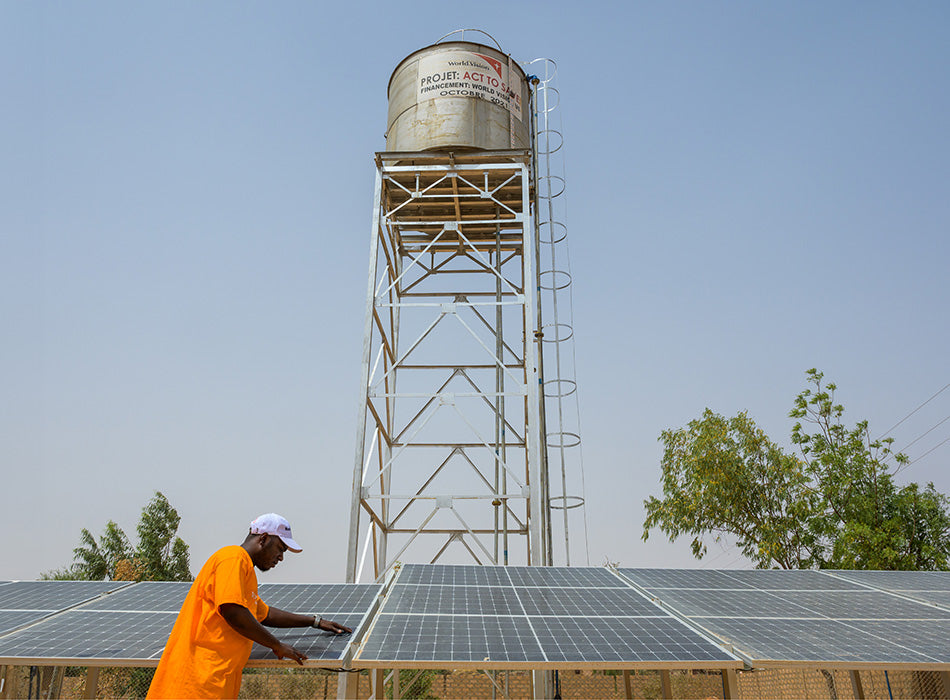 A man wearing a bright orange shirt and white baseball cap examines solar panels.