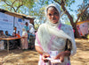 A woman looks at the camera, holding cash. Behind her, people wait in line to receive cash and vouchers.