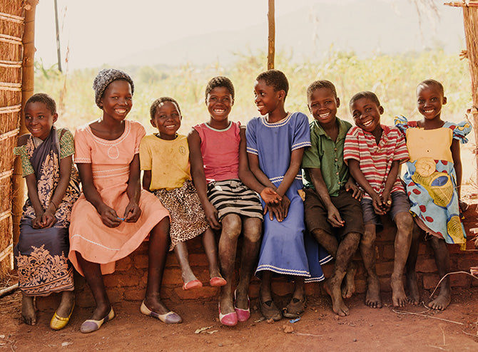 Eight children sitting together on a bench, smiling and laughing.