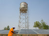 A man wearing a bright orange shirt and white baseball cap examines solar panels.