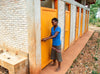A girl wearing a skirt and blue top closes the door to a stall in a bathrom facility.